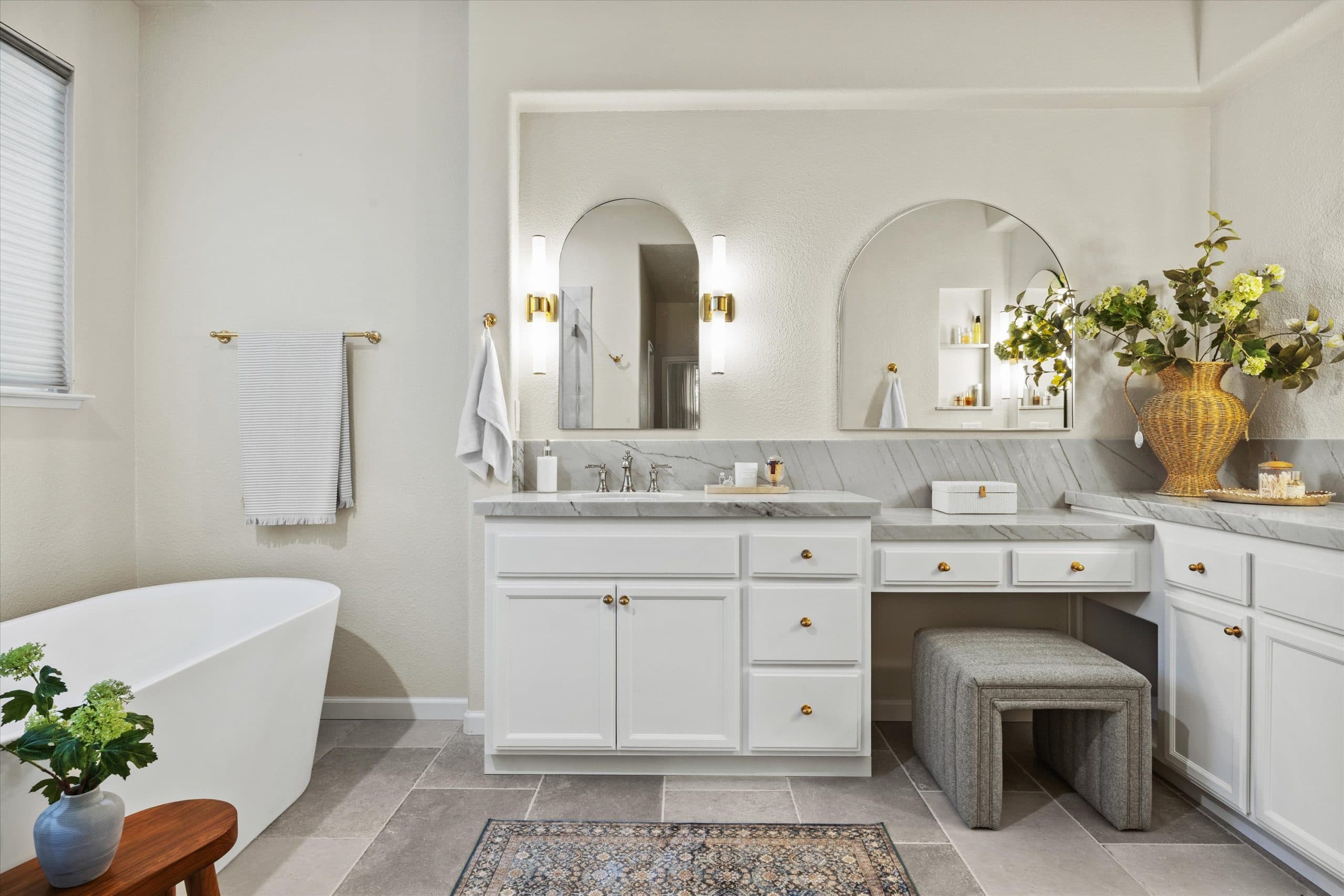 Remodeled dual vanity with white cabinetry, quartzite countertops, and arched mirrors