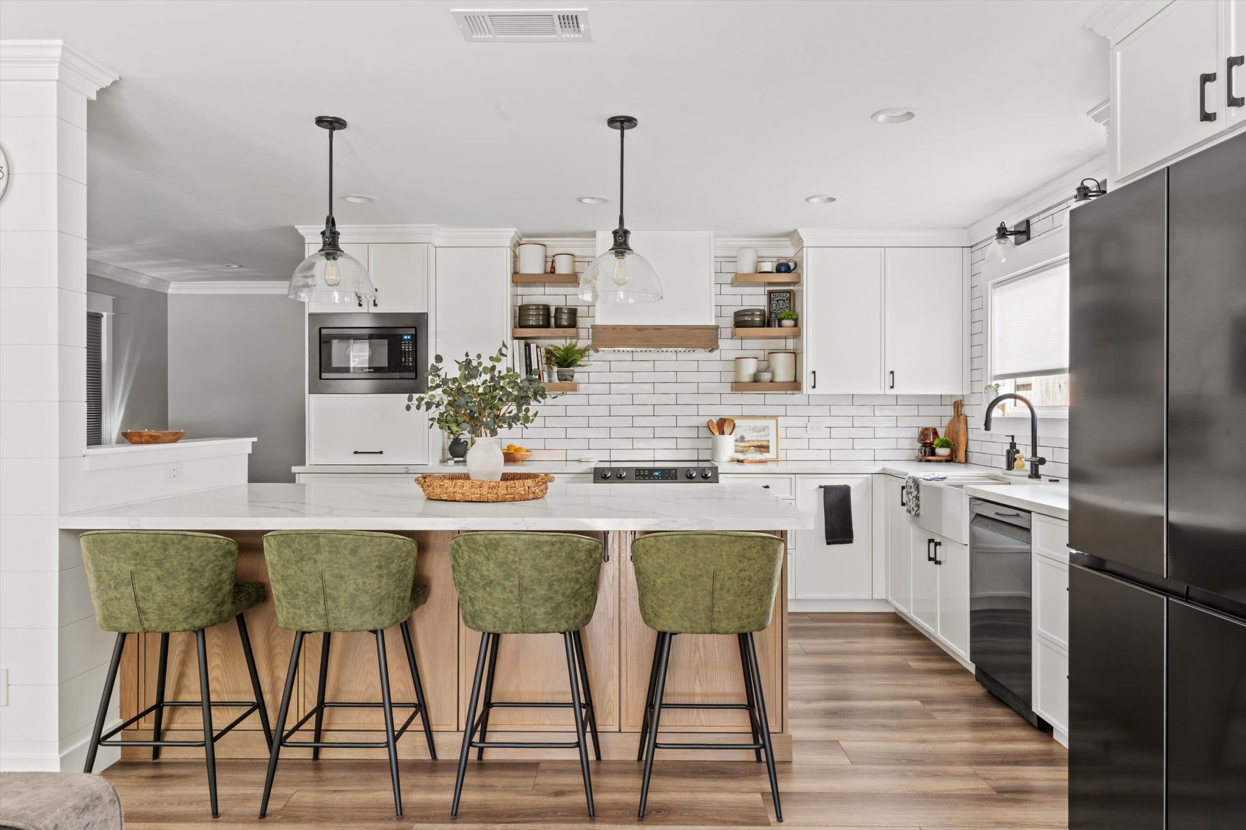 Wide-angle view of remodeled open-concept kitchen with white and natural wood two-tone cabinetry, large center island, black pendant lights, and subway tile backsplash