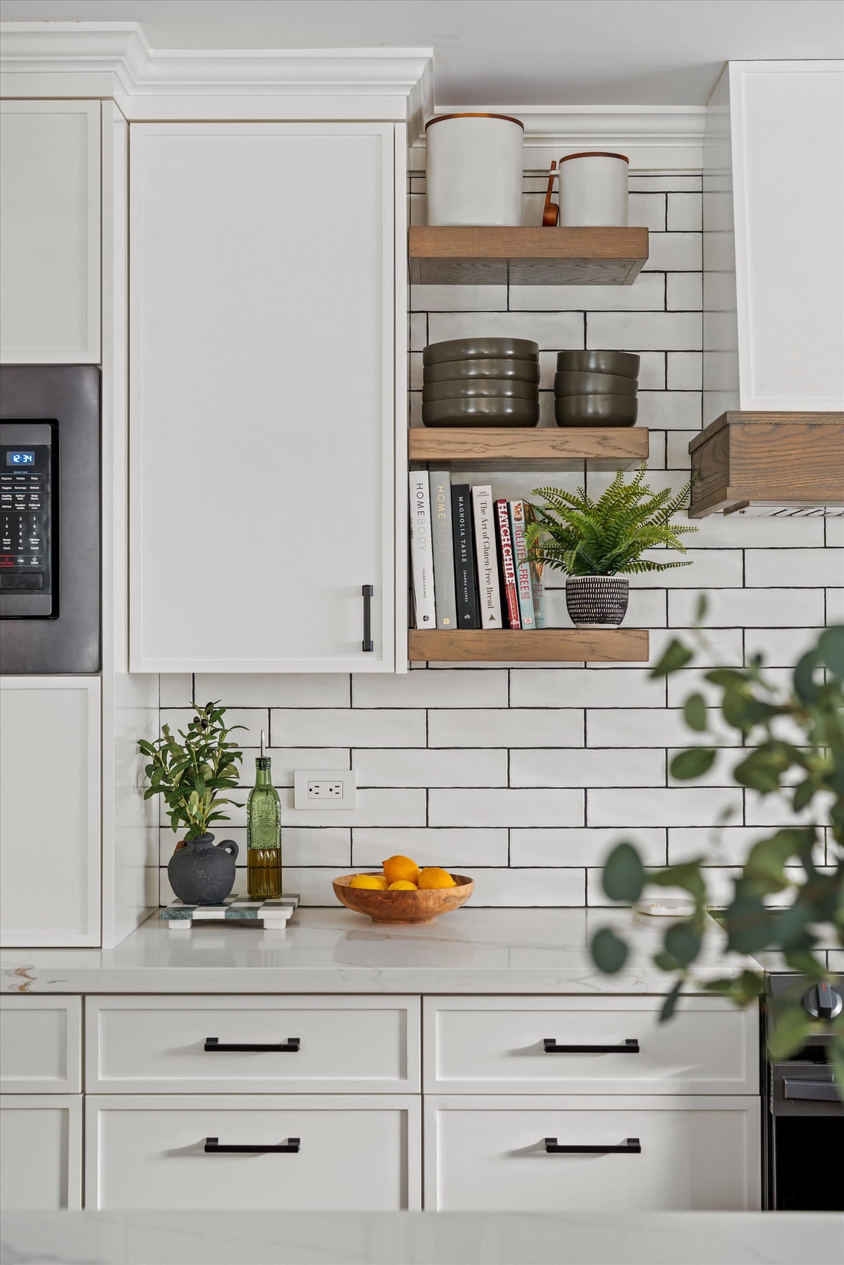 Close-up of kitchen open shelving with styled decor, plants, and storage jars against white subway tile backsplash with natural wood shelf brackets