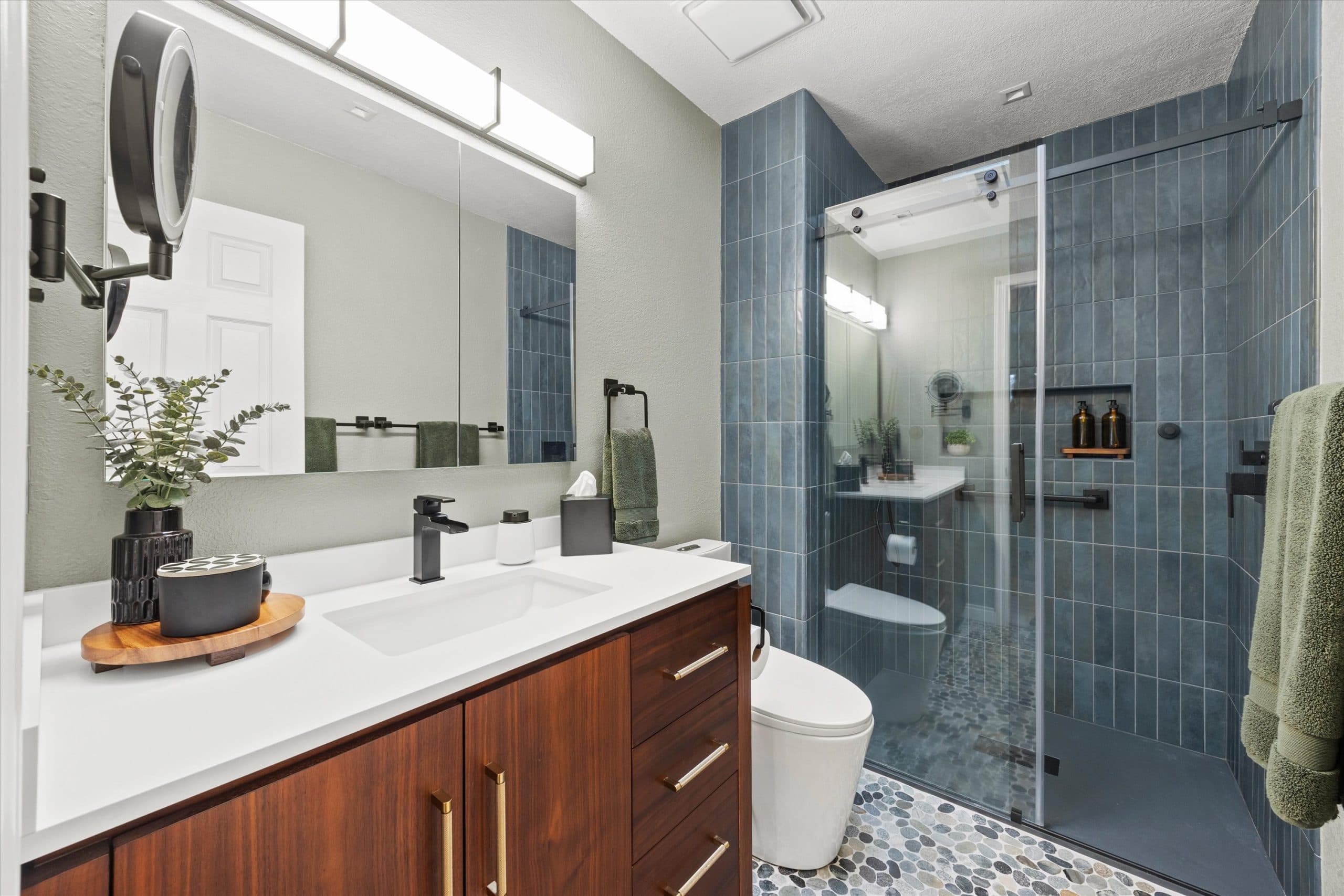 Wide view of remodeled bathroom featuring warm wood vanity, blue subway tile shower, and modern matte black fixtures throughout