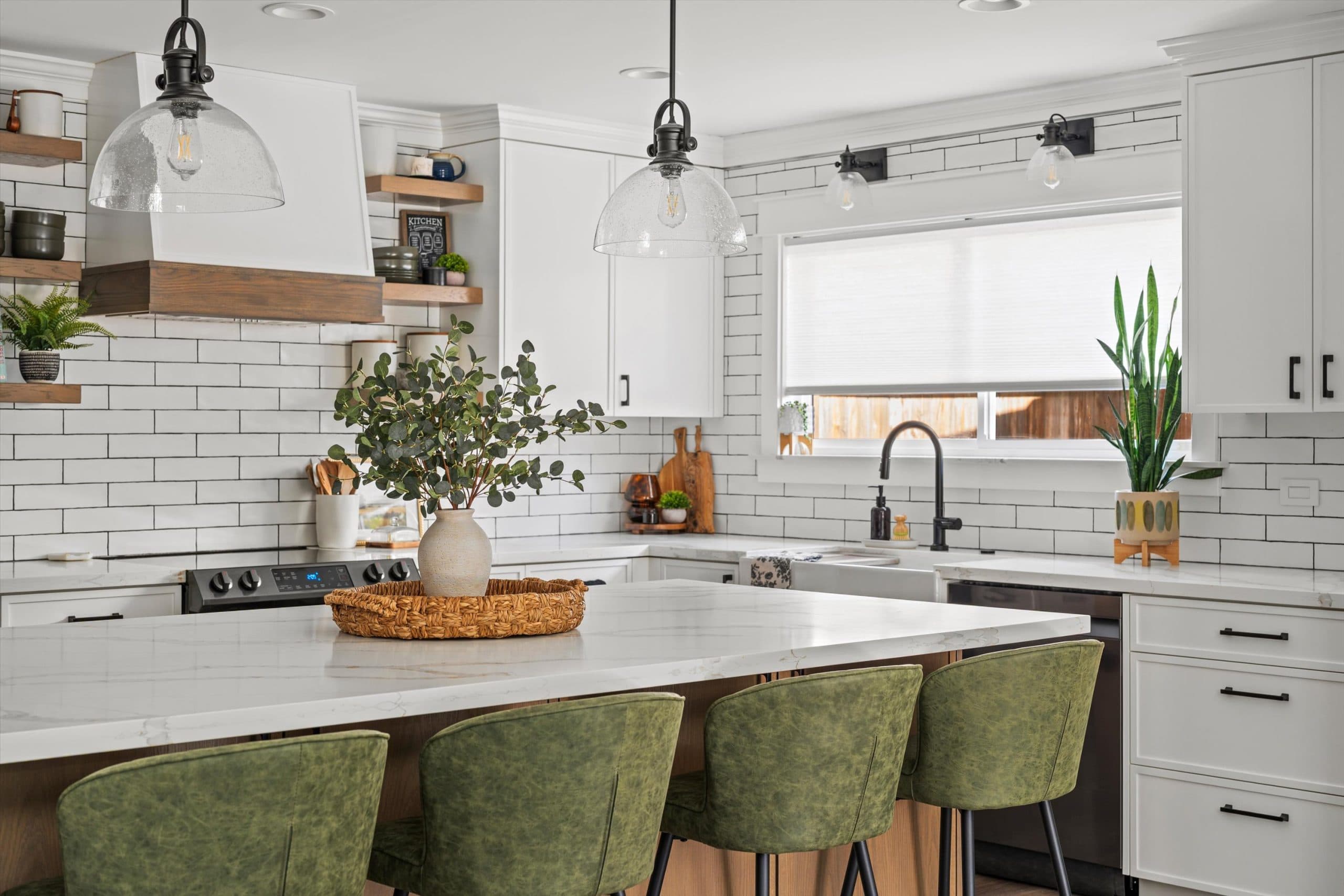 The finished kitchen: white cabinets, subway tile, glass pendants, and a quartz island with four green stools.