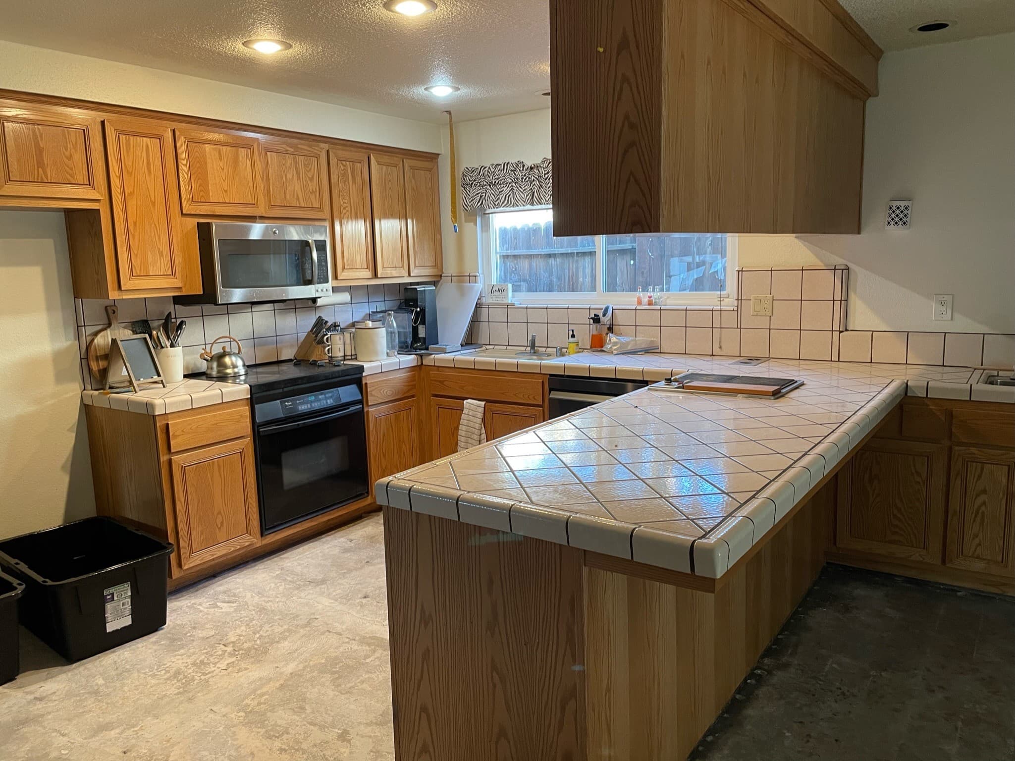 The kitchen before the remodel: oak cabinets, tiled countertops, a peninsula, and a window over the sink.